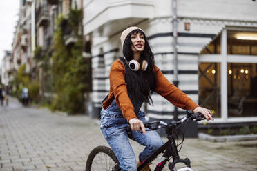 Smiling beautiful woman riding bicycle on footpath near buildings - JCCMF10936