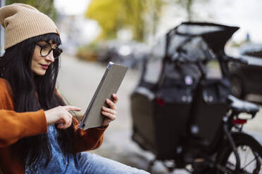 Smiling woman wearing knit hat and using tablet PC - JCCMF10941