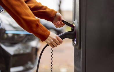 Hands of woman holding electric car charging plug - JCCMF10955