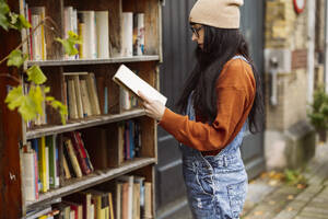 Woman wearing knit hat reading book at bookstore - JCCMF10957