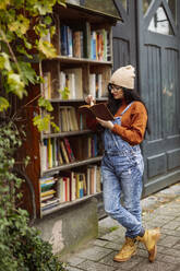Woman wearing beige knit hat reading book at bookstore - JCCMF10959