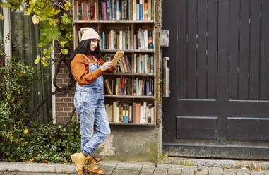 Woman reading book and leaning on stall at footpath - JCCMF10963