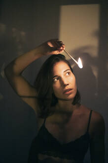 Woman holding ignited matchstick in front of wall - MMPF01075