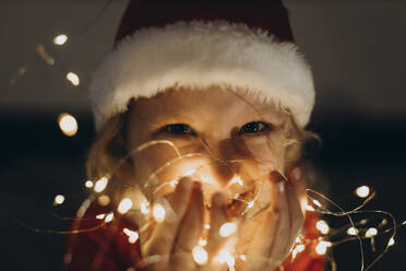 Happy girl wearing Santa hat and holding string lights in hand - SIF01073