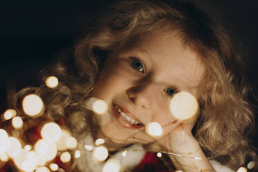 Smiling blond girl looking through string lights - SIF01075
