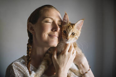 Woman with eyes closed embracing cat at home - ASHF00034