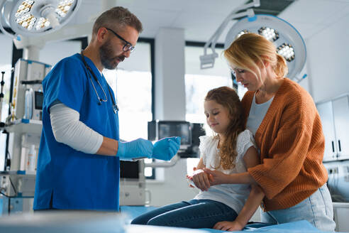 Ein reifer Arzt gibt einem kleinen Mädchen Gips für ihren gebrochenen Arm. - HPIF33724