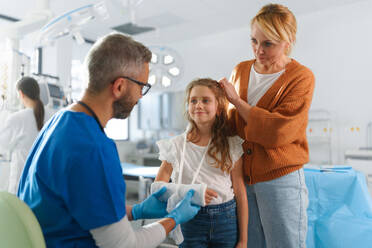 Mature doctor giving gypsum to little girl on her broken arm. - HPIF33745