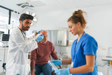 Close-up of doctor and nurse treating injured head of senior man. - HPIF33763