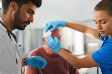 Young doctor and nurse treating injured head of senior man. - HPIF33771