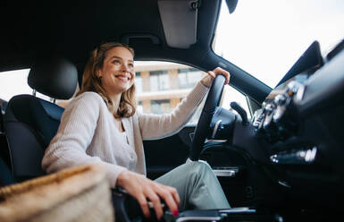 Happy woman driving her new electric car in a city. - HPIF33804