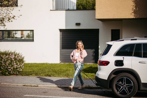 Young woman charging electric car in home, sustainable and economic transportation concept. - HPIF33820