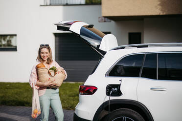 Woman coming back from a grocery store, waiting for car charging. - HPIF33823