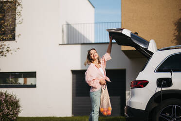 Woman coming back from a grocery store, waiting for car charging. - HPIF33824