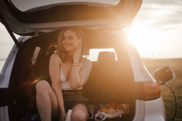 Young woman sitting in a car trunk, waiting for charging it. - HPIF33843