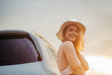 Portrait of young smiling woman standing near the car, enjoying summer time. - HPIF33846