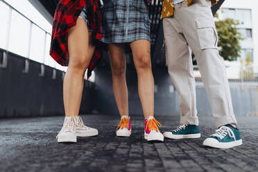 Close-up of young students' legs standing in the city. Zoomers in trendy stylish clothes standing in front of university building. - HPIF33865