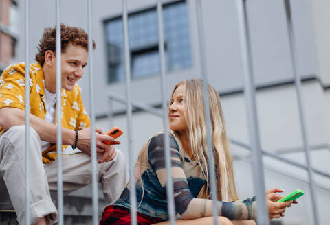 Young Gen Z students meeting outside in the city, sitting on the stairs. Love at first sight. Boy and girl feeling instant attraction. - HPIF33875