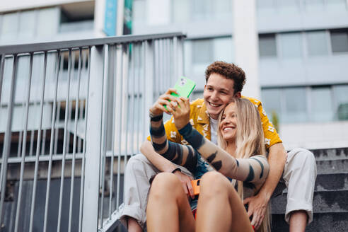 Portrait of generation z couple sitting outdoors in the city and taking selfie. Students spending free time online, watching social media content. Concept of gen Z as loneliest generation. - HPIF33876