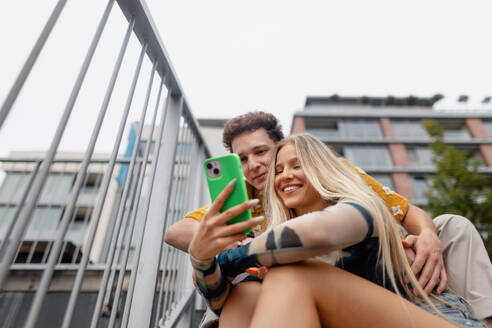 Portrait of generation z couple sitting outdoors in the city and taking selfie. Students spending free time online, watching social media content. Concept of gen Z as loneliest generation. - HPIF33877