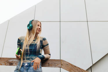 Portrait of a Generation Z girl student listening to music via headphones outdoors in the city. Student spending free time online and alone. Concept of gen Z as loneliest generation. - HPIF33895