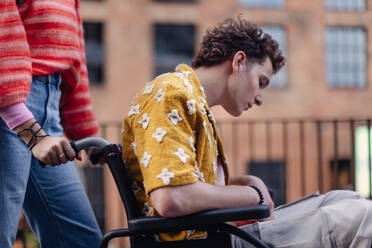 Sad gen Z boy in a wheelchair with friends in the city. Inclusion, equality, and diversity among Generation Z. Sadness and helplessness in the face of chronic illness. - HPIF33908