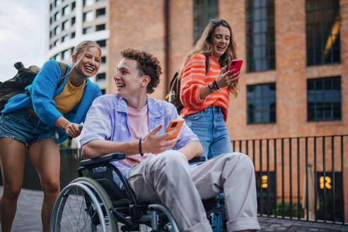 Handsome gen Z boy in a wheelchair with friends in the city. Inclusion, equality, and diversity among Generation Z. - HPIF33910