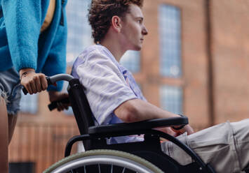 Sad gen Z boy in a wheelchair with friends in the city. Inclusion, equality, and diversity among Generation Z. Sadness and helplessness in the face of chronic illness. - HPIF33911