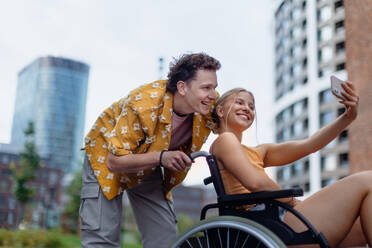 Beautiful gen Z girl in a wheelchair with her boyfriend taking selfie. Inclusion, equality, and diversity among Generation Z. - HPIF33914