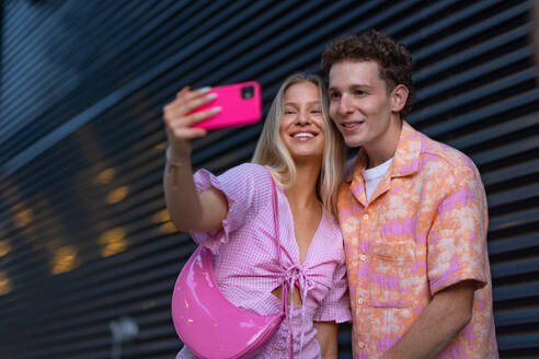 Gen Z couple in pink outfit taking selfie before going the cinema to watch movie. The young zoomer girl and boy watched a movie addressing the topic of women, her position in the world, and body image. - HPIF33919