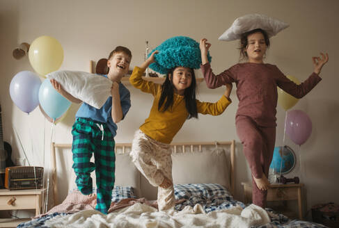 Three happy friends having fun with pillows on bed. - HPIF33931