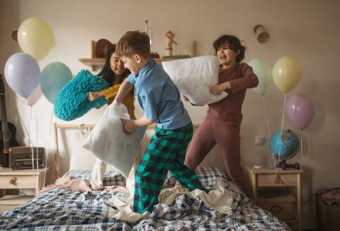 Three happy friends having fun with pillows on bed. - HPIF33932