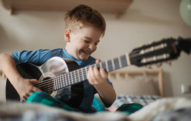 Happy boy playing on the guitar in the room. - HPIF33938