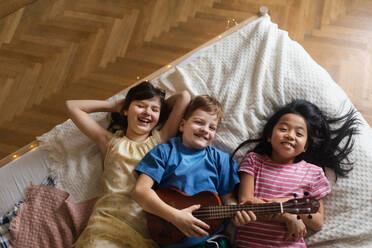 Top view of three happy friends lying in bed with ukulele. - HPIF33961