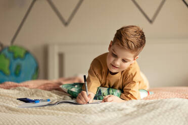 Little boy lying on a bed and doing the homework. - HPIF33988