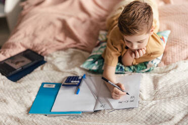 Little boy lying on a bed and doing the homework. - HPIF33989