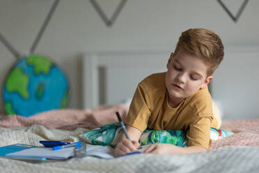Little boy lying on a bed and doing the homework. - HPIF33990