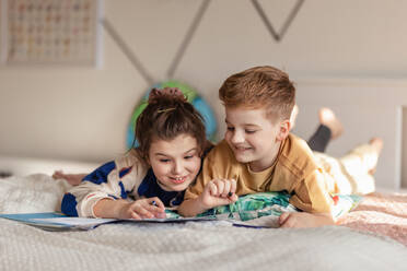 Little children lying on bed and doing their homework. - HPIF33994