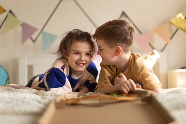 Happy friends lying on a bed and eating a pizza. - HPIF33995