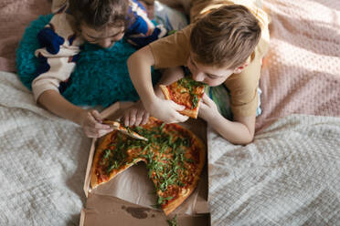 Top view of friends lying on a bed and eating a pizza. Eating food in the bedroom. - HPIF33997