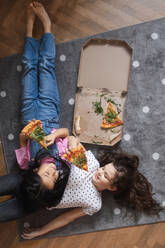 Happy friends lying on a floor and eating a pizza. - HPIF34001