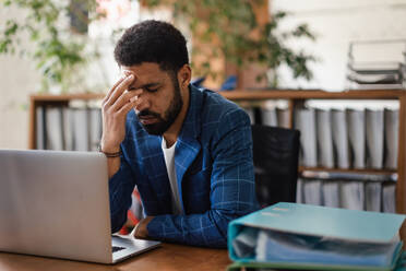 Young exhausted male employee in front of notebook in his office. Signs of burnout at work. - HPIF34022