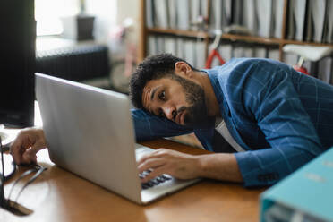 Young exhausted male employee in front of notebook in his office. Signs of burnout at work. - HPIF34024