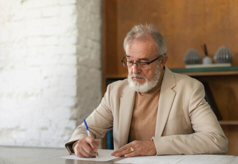Serious eldery businessman signing document at office table. Portrait of senior man, ceo, boss signing a contract. - HPIF34117
