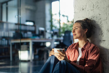 Happy female entrepreneur in her own office drinking coffee. Moment of peace after workday. Woman-owned business. - HPIF34127