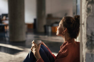 Happy female entrepreneur in her own office drinking coffee and watching sunset. Moment of peace after workday. Woman-owned business. - HPIF34129