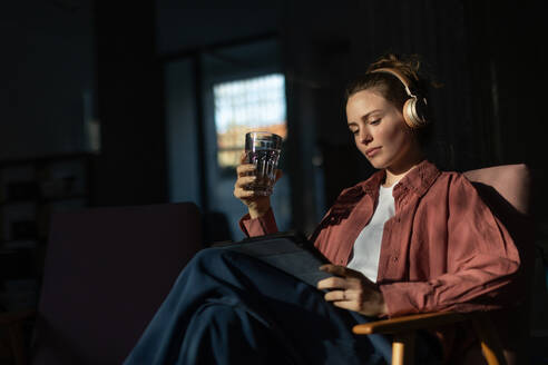 Young woman stting in armchair, listening music and working on a digital tablet. - HPIF34130