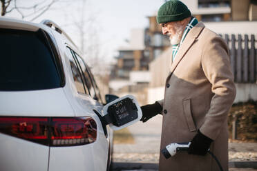 Close up of a senior man charging electric car. - HPIF34140