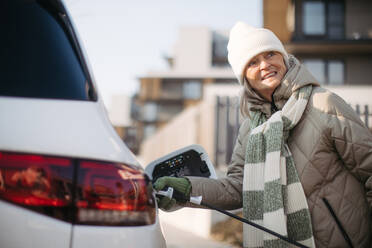 Close up of a senior woman charging electric car. - HPIF34145