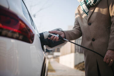 Close up of a senior man charging electric car. - HPIF34149